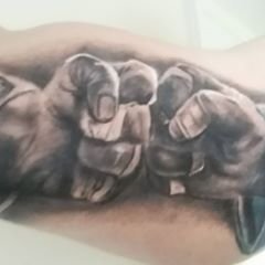 Close-up of a detailed black and grey tattoo depicting two clenched fists on an arm.