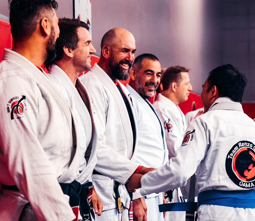 Group of men in martial arts uniforms shaking hands and smiling in a gym setting.