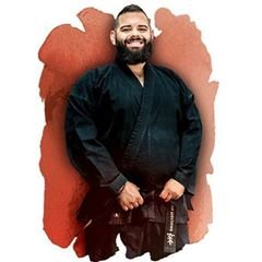 Smiling man with a beard wearing a black martial arts gi holding a black belt.