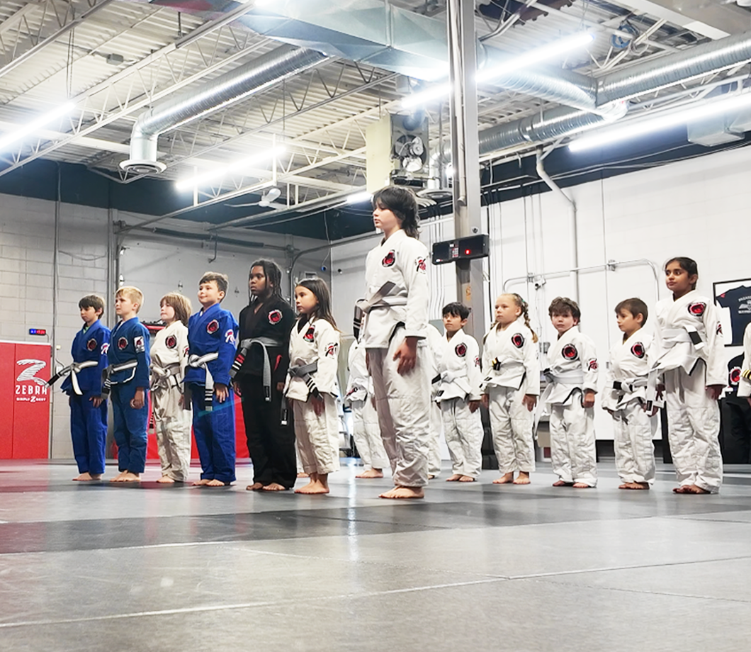 Group of children in martial arts uniforms standing in line on a gym floor.