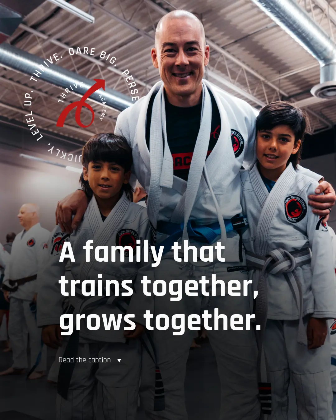 Smiling adult and two children in martial arts uniforms posing together in a gym with others training in the background.